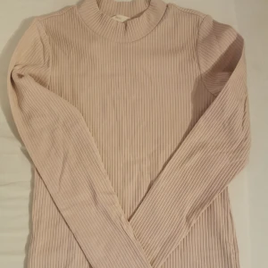 Ljusrosa ribbad långärmad tröja - Supersnygg ljusrosa ribbad tröja från H&M. Tröjan har lång ärm, rund halsringning och är i ett mjukt, stretchigt material som sitter skönt på kroppen. Perfekt att styla med jeans eller kjol för en clean look.