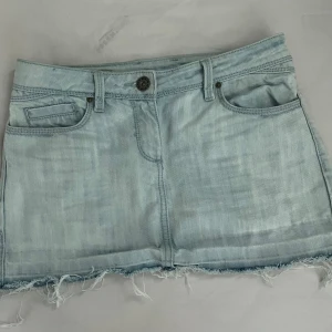 Ljusblå jeanskjol  - Ljusblå  jeanskjol med låg midja och slitningar lägst ner. Oanvänd men köpt second hand, men utan defekter. Står strl 36 men för liten för mig, mer 32/34