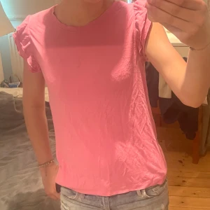 Rosa topp med volangärmar - Supersöt rosa topp med volangdetaljer på ärmarna. Passar mellan storlekarna xs och M den här dock en liten fläck fram på tröjan men syns knappast.