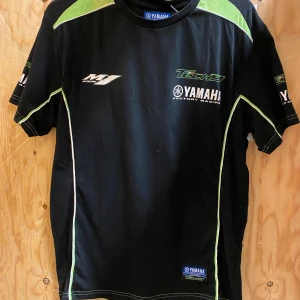 Yamaha T-shirt - Svart Yamaha Factory Racing t-shirt med gröna och vita detaljer samt Tech3-logga. Snygga tryck på bröst, rygg och ärmar. Klassisk passform med rund hals och korta ärmar. Perfekt för dig som gillar racing och vill sticka ut med sportig stil. Fint skick och Priset är prutbart!