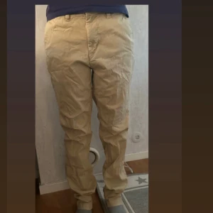 Beiga chinos med raka ben - Säljer ett par klassiska beiga chinos med raka ben och normal passform. Byxorna har bälteshällor, knapp- och dragkedjegylf samt bakfickor med knappar. Perfekta för en clean och avslappnad stil. Jag är 163