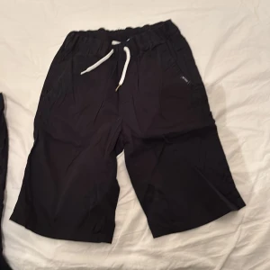 Svarta shorts från KappAhl med snörning - Svarta shorts från KappAhl med elastisk midja och vit snörning framtill. Shortsen har fickor både fram och bak samt en liten etikett på baksidan. Perfekta för sommardagar.