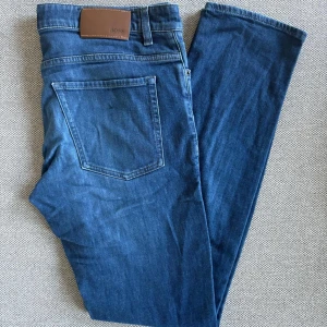 Blå jeans från BOSS - Säljer ett par klassiska blå jeans från Boss Jeansen har en snygg läderpatch med BOSS-logga bak i midjan och är tillverkade i mjukt denimtyg. Perfekta för dig som gillar stilrena och tidlösa jeans.