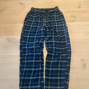 Rutiga mjukisbyxor i blått och svart - Mysiga mjukisbyxor med blått och svart rutmönster. Byxorna har resår i midjan och är raka i modellen, perfekta för chill eller hemmakvällar.  Skicka ett meddelande för frågor, storlek, mått osv. 