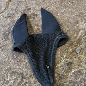 Svart ridhuva med långa öron - Svart ridhuva med långa, mjuka öron och virkad mesh över huvudet. Perfekt för att skydda hästens öron mot insekter under ridning. Klassisk och stilren design.
