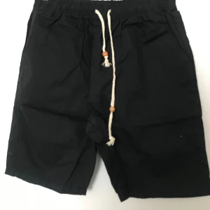 Svarta shorts med snörning - Svarta shorts med vit snörning och trädetaljer i midjan. Modellen har elastisk midja och sidofickor, samt en bakficka. Perfekta för sommaren och enkel stil. Stlk kvar M-3XL 