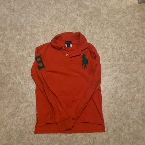 Orange Långärmad tröja från Polo Ralph Lauren - En orange långärmad Polo Ralph Lauren tröja som är i ganska bra skick. Använd några gånger men är fortfarande i bra skick. Skriv till mig om ni har nån fråga eller nått om tröjan tröjan  eller om storlek för jag vet inte exakt vad storleken på tröjan är!