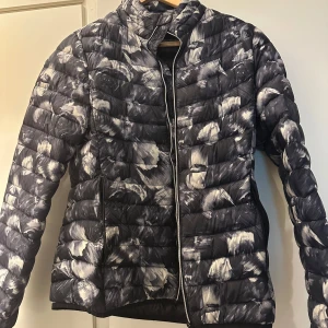 Svart och vit mönstrad dunjacka från Everest - Säljer en svart och vit dunjacka från Everest med abstrakt mönster. Jackan har dragkedja framtill och hög krage. Perfekt för kyliga dagar och har en lätt, puffig känsla.
