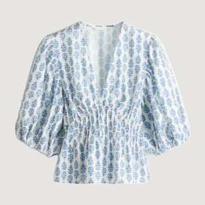 Vit och blå blus med puffärmar - Säljer en söt blus i vitt med blått mönster och v-ringning. Blusen har puffiga trekvartsärmar och smockad midja som ger en fin siluett. Den är slut såld på hm💞har aldrig använt och prislappen är kvar!!