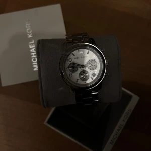 Silverfärgad klocka från Michael Kors - Stilren klocka från Michael Kors i silverfärg med länkarmband och rund urtavla. Helt oanvänd. Perfekt accessoar för att lyfta din outfit.
