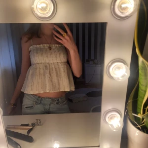 Topp - Säljer en söt vit croppad linnetopp och lätt volang nedtill. Toppen har ett diskret randigt mönster i guld och smockad överdel för en bekväm passform. Perfekt för varma dagar!den är från gina young