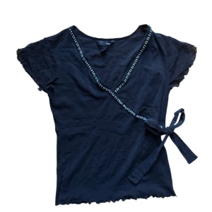 Vintage Svart omlottopp med pärldetaljer från H&M - Svart omlottopp från H&M med v-ringning och sten liknande pärlor längs kanten. Strl M men mer en XS-S i storlek. 