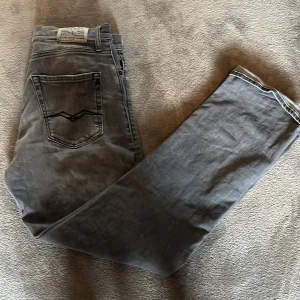 Grå jeansbyxor från Replay - Säljer ett par grå jeansbyxor från Replay, modell Thad. Byxorna har raka ben, klassisk femficksdesign och detaljerade bakfickor. Perfekta för dig som gillar en stilren och enkel look. Storlek 14 år 158cm men skulle säga att de passar större. Aldrig använda.