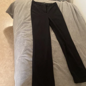 Svarta kostymbyxor från Vero Moda - Klassiska svarta kostymbyxor från Vero Moda med raka ben och hällor för bälte. Byxorna har en stilren design och passar perfekt till en dressad look. Materialet känns mjukt och följsamt.