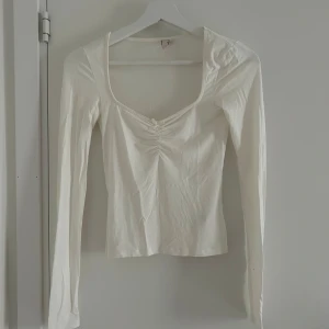 Vit långärmad topp från Nelly - Säljer en vit långärmad topp från Nelly i storlek XXS. Toppen har en djup v-ringning och rynkdetalj framtill vid bysten. Perfekt att styla med jeans eller kjol för en enkel och snygg look.