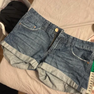 Blå jeansshorts med uppvik - Säljer ett par klassiska blå jeansshorts från Mossimo med uppvikta benslut och femficksmodell. Shortsen har normal passform och stängs med dragkedja och knapp. Perfekta för varma dagar!
