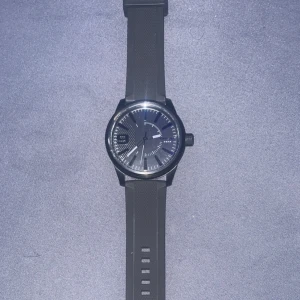 Diesel Herrklocka DZ1807 - Snygg svart herrklocka från Diesel, modell DZ1807. Klockan har en rund urtavla med tydliga markeringar och ett svart armband i gummi. Modern och stilren design med Diesel-logga på urtavlan.