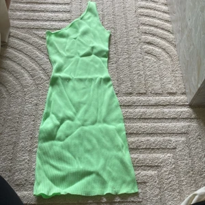 Grön ribbad one shoulder klänning från Bershka - Säljer en ljusgrön ribbad klänning från Bershka med one shoulder-design. Klänningen är figurnära och har en snygg, enkel stil som sticker ut med sin fräscha färg. Perfekt för dig som vill ha något trendigt och bekvämt.