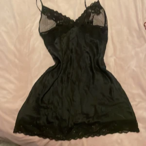 Svart spetsnattlinne med tunna band - Snyggt svart nattlinne i silk med tunna axelband och detaljer i spets och mesh upptill. Nattlinnet har en feminin passform och spetskant längst ner för extra stilpoäng. Perfekt för dig som gillar en elegant och bekväm look.