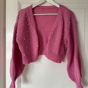 Rosa croppad kofta med pärlor - Superfin rosa croppad kofta från SHEIN med pärldetaljer framtill. Stickad modell med långa ärmar och bred ribbad mudd vid ärmslut och nederkant. Perfekt för att liva upp outfiten med en söt touch!