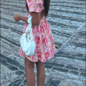 Blommig kortklänning med puffärm och öppen rygg - Superfin kortklänning med rosa och röda blommor, puffärmar och öppen rygg. Klänningen har en söt, romantisk stil och är perfekt för sommarens alla tillfällen. Materialet känns lätt och luftigt.