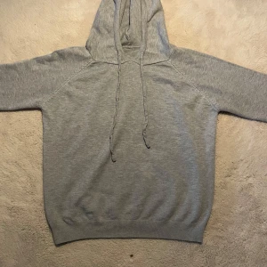 Ljusgrå hoodie - En enkel och stilren ljusgrå hoodie med huva och dragsnören. Tröjan har långa ärmar och ribbade muddar vid ärmslut och nederkant. Perfekt för en avslappnad look. Passar xxs och xs 