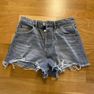 Grå jeansshorts från Zara  - Snygga grå jeansshorts med fransiga kanter och hög midja. Klassisk femficksmodell med knappar framtill. Perfekta för sommaren och ger en avslappnad vibe.