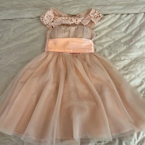 Ljusrosa spetsklänning från Eva & Lola - Superfin ljusrosa klänning från Eva & Lola med spets upptill, avtagbart satinband i midjan och voluminös tyllkjol. Klänningen har vackra spetsdetaljer vid axlarna och en romantisk känsla, perfekt för speciella tillfällen.