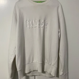 Hugo Boss sweatshirt  - Vit sweatshirt från Hugo Boss med broderad logga på bröstet. Tröjan har rund halsringning, ribbade muddar och normal passform. Perfekt för en stilren och enkel look.