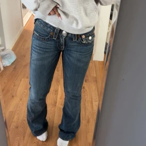 Mörkblå bootcut jeans från True Religion - Säljer ett par mörkblå jeans från True Religion med bootcut passform. Jeansen har kontrastsömmar, silverfärgade knappar och detaljerade fickor både fram och bak, har även låg midja 