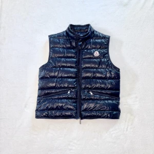 Mörkblå dunväst från Moncler - Snygg svart dunväst från Moncler med hög krage och dragkedja framtill. Västen har två fickor med dragkedja och Moncler-logga på bröstet. Ruggigt skön modell! Moncler size 2 (s/m). Har du några funderingar eller frågor så är du mer än välkommen att skriva till mig! 