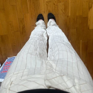 Vita randiga linnebyxor - Säljer ett par vita linnebyxor med tunna beigea ränder. Byxorna har mid midja och en rak, loose passform som ger en avslappnad look. Perfekta för varmare dagar och enkla att matcha med olika toppar. Det står inte vilken storlek på byxan, jag är 165 och de är lite långa på mig. Har normalt sett xs/s i kläder