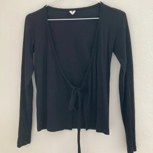 Svart långärmad omlottröja - Svart långärmad topp med djup v-ringning och omlottl. Enkel och stilren design som passar till många olika outfits. Mjuk och stretchig känsla. Från Arket