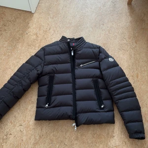 Souillet Short Down Biker Jacket Moncler - Säljer en svart dunjacka från Moncler med ståkrage och tre fickor med dragkedja. Jackan har Moncler-logga på ärmen och quiltad design. Perfekt för kyliga dagar. Nypris 17.580 Storlek M men liten i storlek kan passa xs och s, oanvänd och kvitto finns
