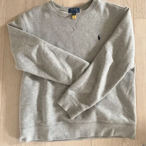 Grå sweatshirt från Polo Ralph Lauren - Storlek: L (14-16 år) / Klassisk grå sweatshirt från Polo Ralph Lauren med rund halsringning och broderad logga på bröstet. Tröjan har långa ärmar och är tillverkad i mjuk bomullsmix, perfekt för en avslappnad stil. Säljes då denna är för liten för mig! 