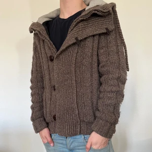 Cardigan - Mysig brun stickad jacka med huva och stora knappar framtill. Jackan har ribbade detaljer och är helfodrad med mjukt tyg på insidan av huvan. Den är inte så varm som den ser ut, perfekt vår jacka.