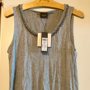 *NY*Grått linne med smyckad halsringning från Vila i stl S - Ljusgrått/melerat längre linne med pärlband i silver runt ringningen. Stl S, ngt oversize, mkt mjukt och tunt material, perfekt för sommardagar.  Inget att anmärka på.   Nypris: 249 sek, Pris nu: 40 sek  