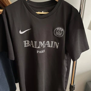 Svart t-shirt från Balmain x Paris - Snygg svart t-shirt med Balmain Paris-tryck och Paris-märke på bröstet. Påsar och tags finns kvar. 
