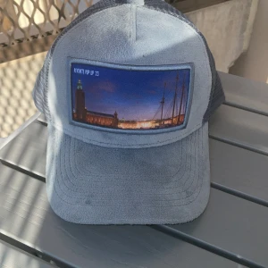 Ljusblå keps med fototryck från Revenite - Snygg ljusblå keps från Revenite med mesh baktill och ett fototryck av Stockholms stadshus framtill. Kepsen har böjd skärm och justerbar passform. Perfekt för sommarens alla äventyr. Köpt i pop-up butiken för 499krAnvänd högst 3 gånger. Pris kan diskuteras