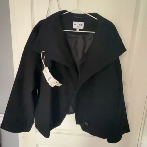 Svart kappa med bred krage - Säljer en svart kappa med bred krage och dubbelknäppning. Jackan har en oversized passform och långa ärmar. Perfekt för dig som gillar stilrena och minimalistiska plagg. Fråga om mer bilder. Den e helt oanvänd med prislapp kvar. Pris kan diskuteras 