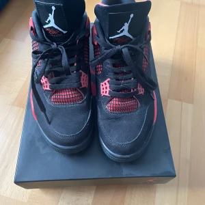 Nike Air Jordans 4 Retro svart/röd - Säljer ett par Nike Air Jordans 4 Retro i svart och rött. Skorna har klassisk siluett med snörning, meshpaneler och Jumpman-logga på plös och häl. Ovandelen är i mocka och syntet, med platt sula och rund tå.
