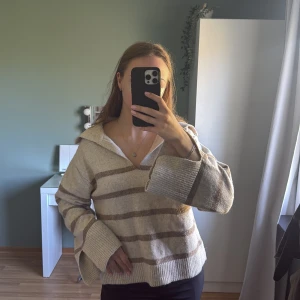 Beige och vit randig stickad tröja från Gina Tricot - Mysig stickad tröja från Gina Tricot i beige och vitt med breda ränder. Tröjan har v-ringning, långa ärmar och en avslappnad passform. Perfekt för lager-på-lager och chill dagar.