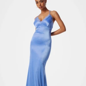 Ljusblå långklänning i satin med spetsdetaljer - Elegant ljusblå långklänning i satin med smala axelband som korsas i ryggen. Klänningen har v-ringning och spetsdetaljer längs urringningen, samt en figurnära passform som framhäver siluetten. Bara använd en gång! 