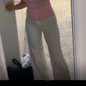 Vita vida byxor med hög midja - Säljer ett par vita byxor med hög midja och vida ben. Byxorna har en slät front och är perfekta för en stilren look. Passar dig som gillar en trendig och bekväm passform.