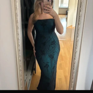  långklänning med svart spetsdetalj - Säljer en elegant ljusblå undertill  långklänning med svarta spetsdetaljer och figurnära passform. Sjukt fin helt ny med prislapp. Storlek S. Köpt i USA så är garanterad att ingen kommer ha likadan. 