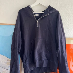 Svart hoodie med dragkedja från Acne - Säljer en svart hoodie från Acne med halv dragkedja framtill och stor huva. Tröjan har en klassisk känguruficka och långa ärmar. Perfekt för en avslappnad stil.