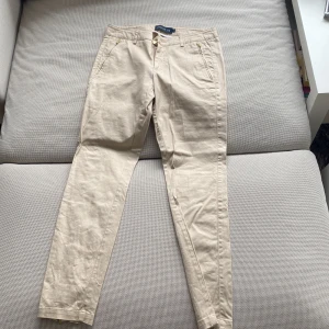 Beiga byxor från Stockhlm - Snygga beiga byxor från Stockhlm med normal passform och raka ben. Byxorna har fickor fram samt stängs med dragkedja och knapp. Perfekta till vardags och enkla att matcha med olika toppar. (För små för mig)