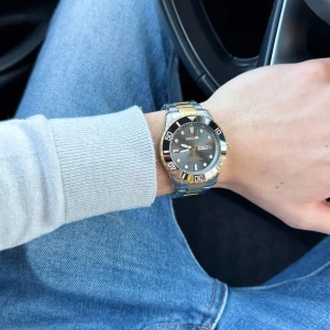 Tvåtonad sportig herrklocka  - Säljer en snygg herrklocka från klockmärket Champion med tvåtonad länk i silver och guld. Urtavlan är svart med tydliga index och datumvisning. Klockan har en robust boett och vridbar bezel, perfekt för dig som gillar stilrena accessoarer. Liten repa på glaset finns!