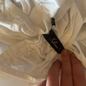 Vit kortklänning från S. Oliver - Supersöt vit kortklänning från S. Oliver med puffärmar och volanger. Klänningen har en fyrkantig ringning och är tillverkad i ett lätt material som passar perfekt för varma dagar.