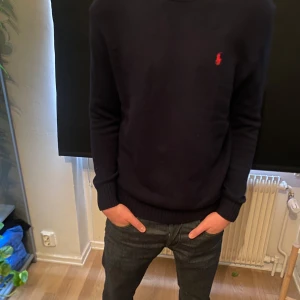 Mörkblå stickad tröja från Ralph Lauren - Säljer en stilren mörkblå tröja från Ralph Lauren med den klassiska röda loggan broderad på bröstet. Tröjan har rund halsringning och långa, smala ärmar med ribbade muddar. Tveka inte för att skriva vid minsta funderingar!